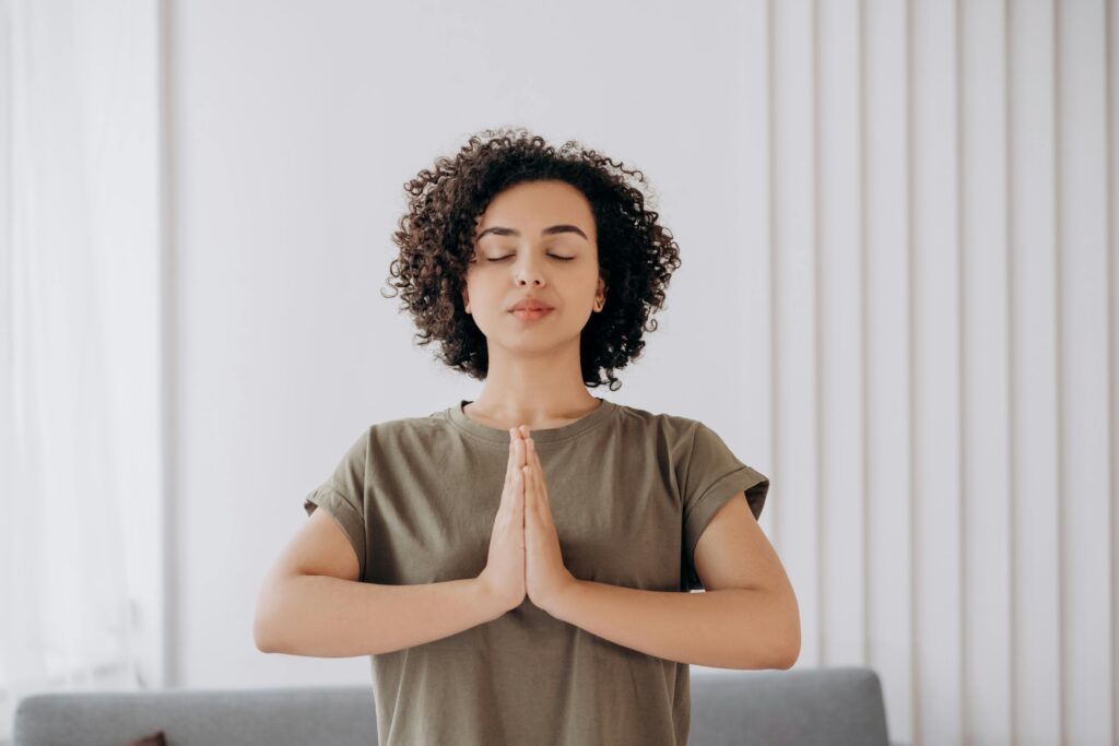 Young woman with curly hair meditates indoors, embracing tranquility and mindfulness.