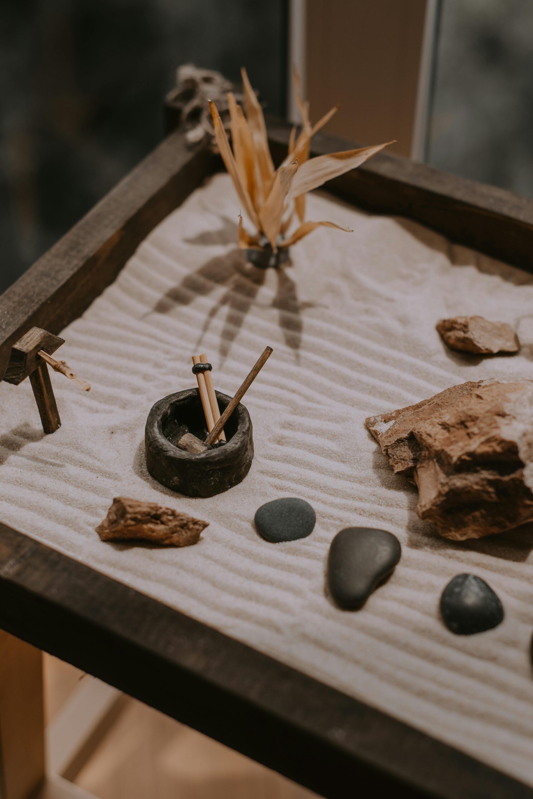 A detailed tabletop zen garden featuring sand, stones, and dried leaves for relaxation and meditation.
